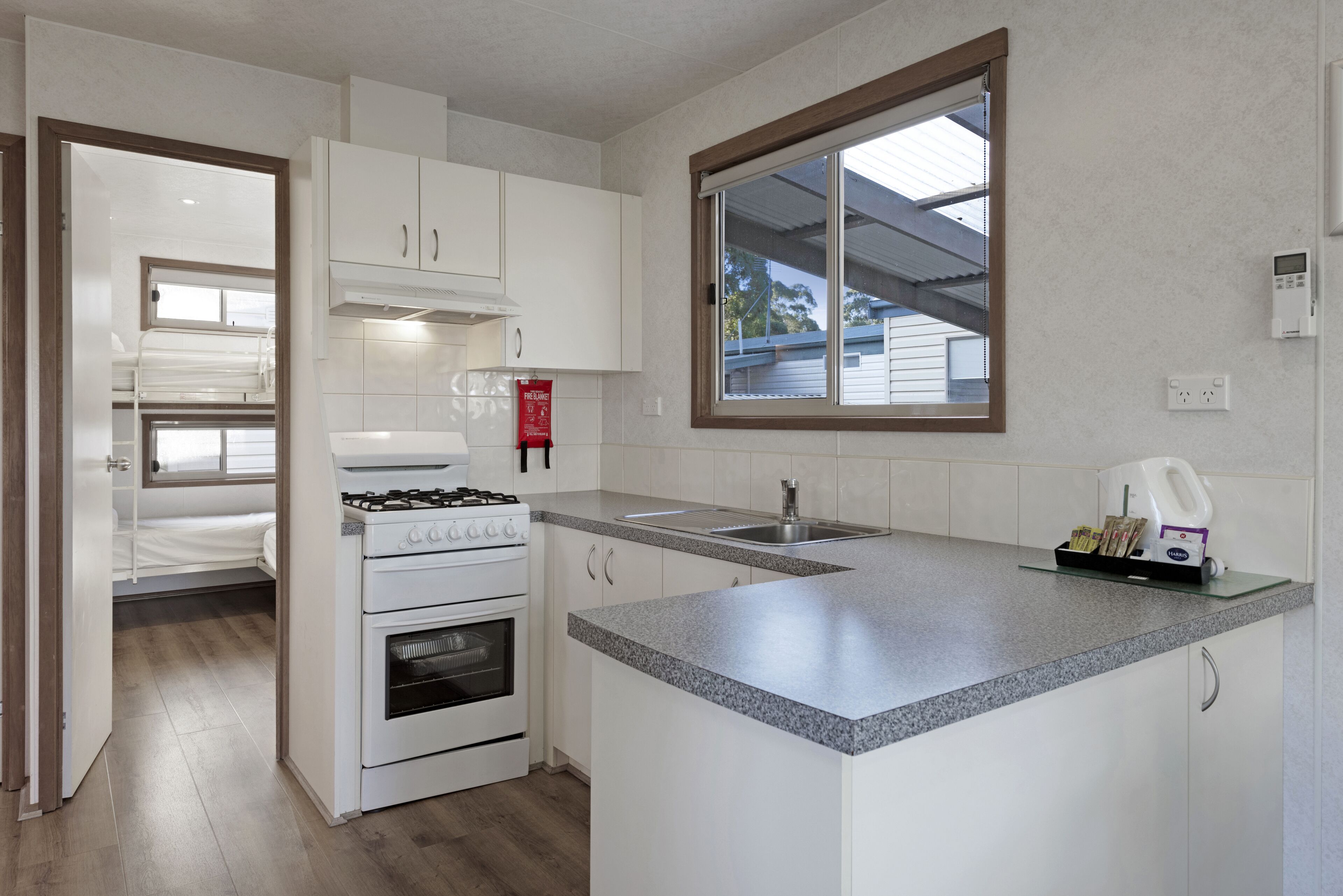 Una cocina compacta con muebles blancos, una estufa integrada y un ventanal sobre el lavamanos.
