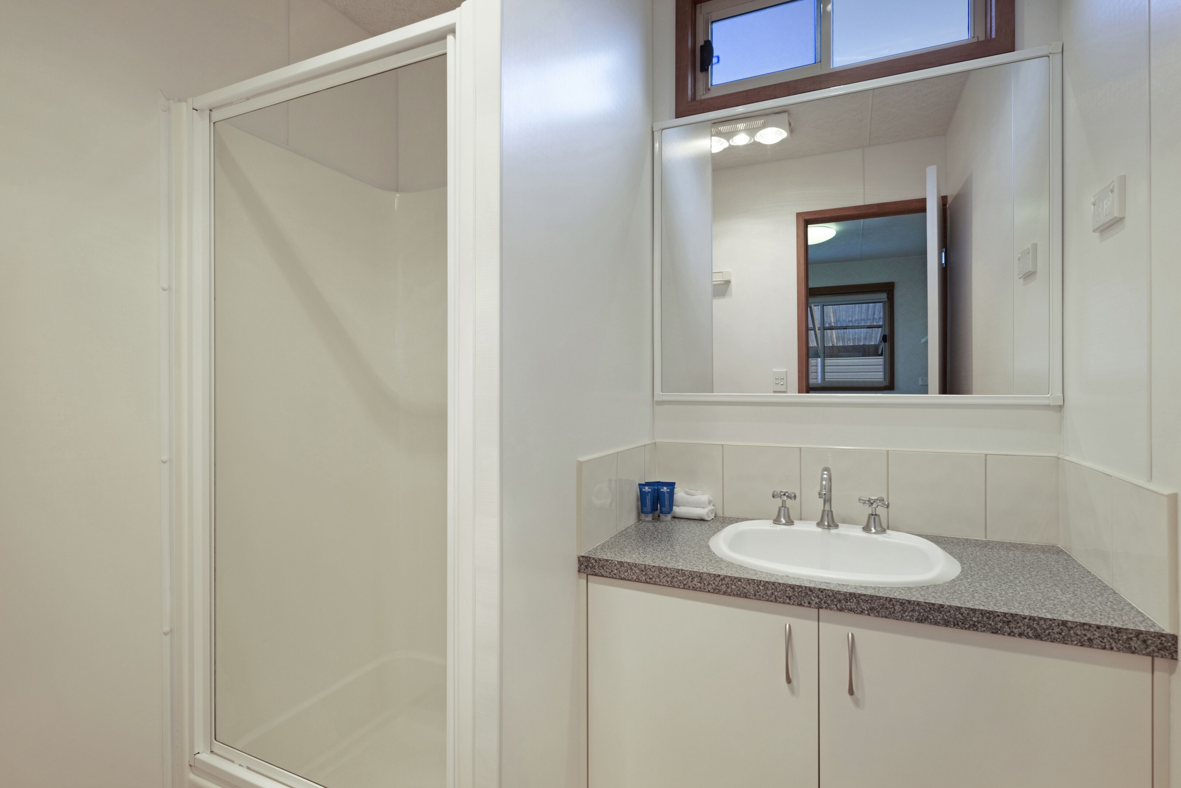 A modern bathroom with a glass shower enclosure, a white sink, and a mirror above it.