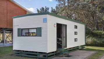 Une maison mobile de plain-pied, avec une porte et des fenêtres vertes, portant le numéro 214, située sur une pelouse, avec un bâtiment en bois en arrière-plan.