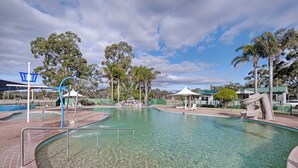 A clear swimming pool with a slide, lounge chairs, and a pavilion. - Discovery Parks - Eden (Boydtown)