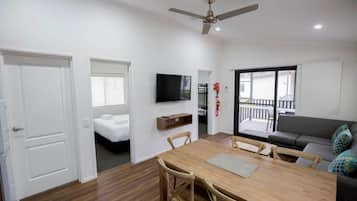 A modern living room with a wooden dining table, a sofa, a TV mounted on the wall, and a balcony with a railing.