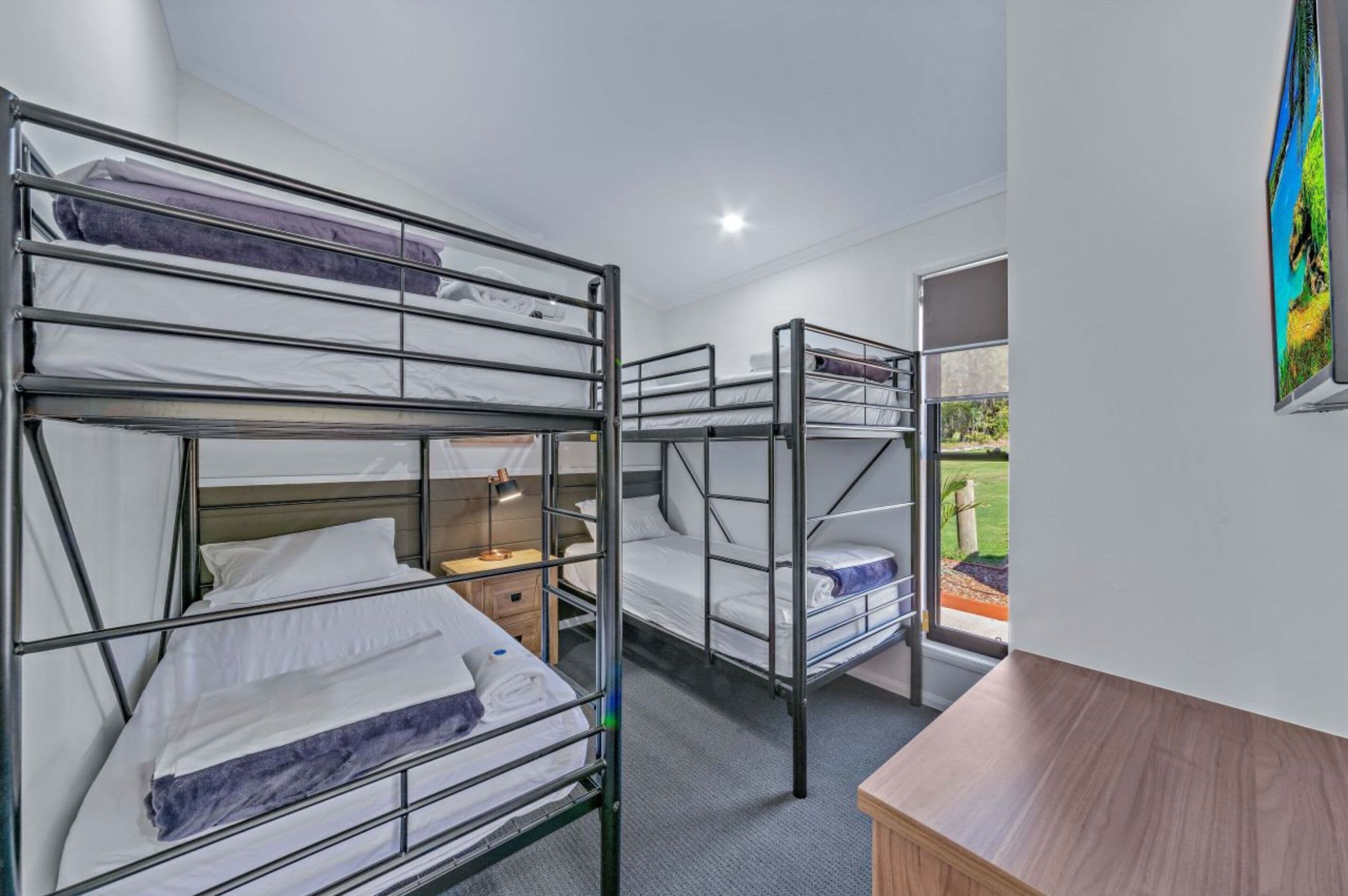A dormitory room with bunk beds, a desk, a lamp, and a view of the outdoors.