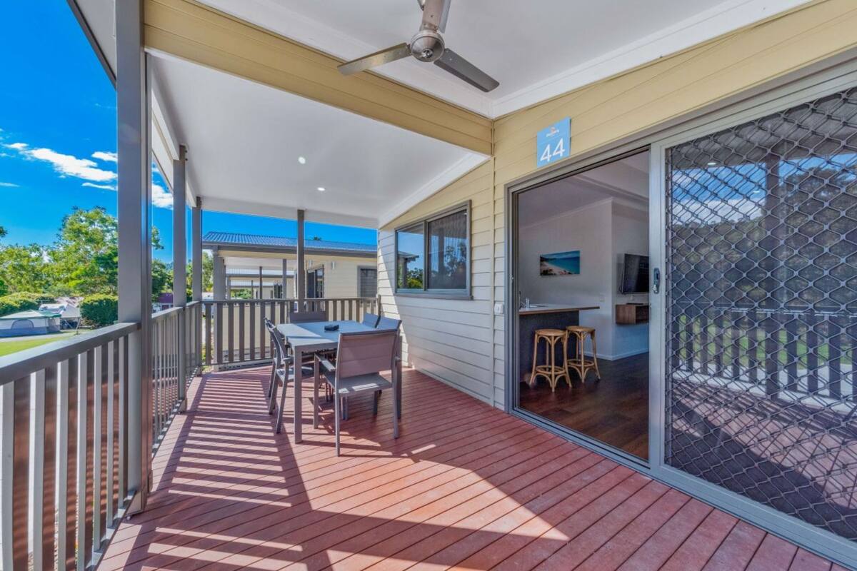 A covered outdoor area with a table and chairs, a ceiling fan, and a sliding glass door leading to an interior space.