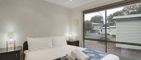 A hotel room with a bed, bedside tables, a ceiling fan, and a large window with a view of the outside.