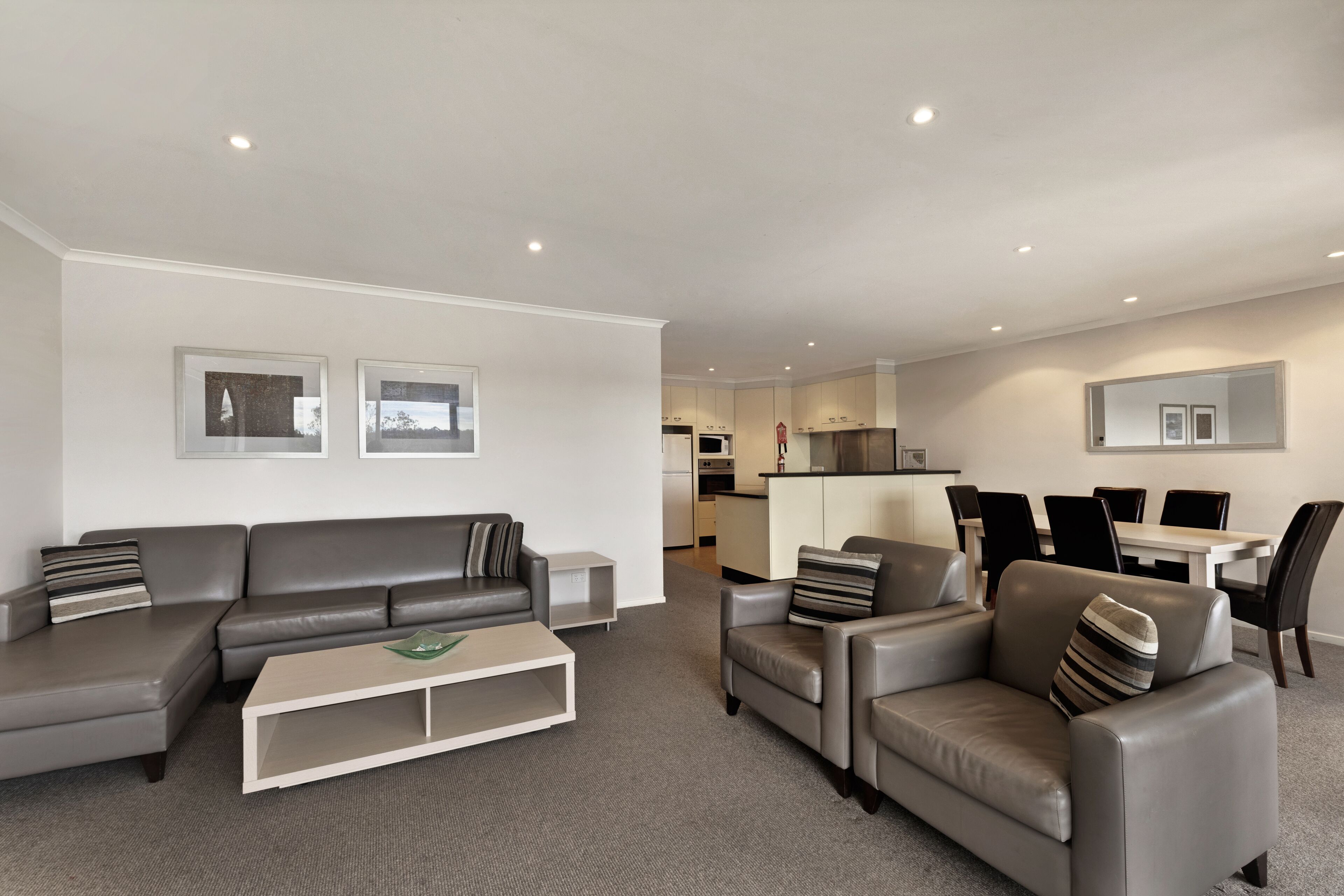 A modern living room with a grey sectional sofa, a white coffee table, and a dining area with a white table and black chairs.
