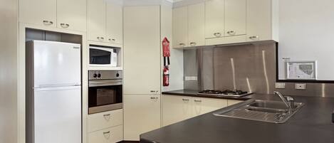 A modern kitchen with white cabinets, a stainless steel refrigerator, an oven, a microwave, a gas stove, and a sink.