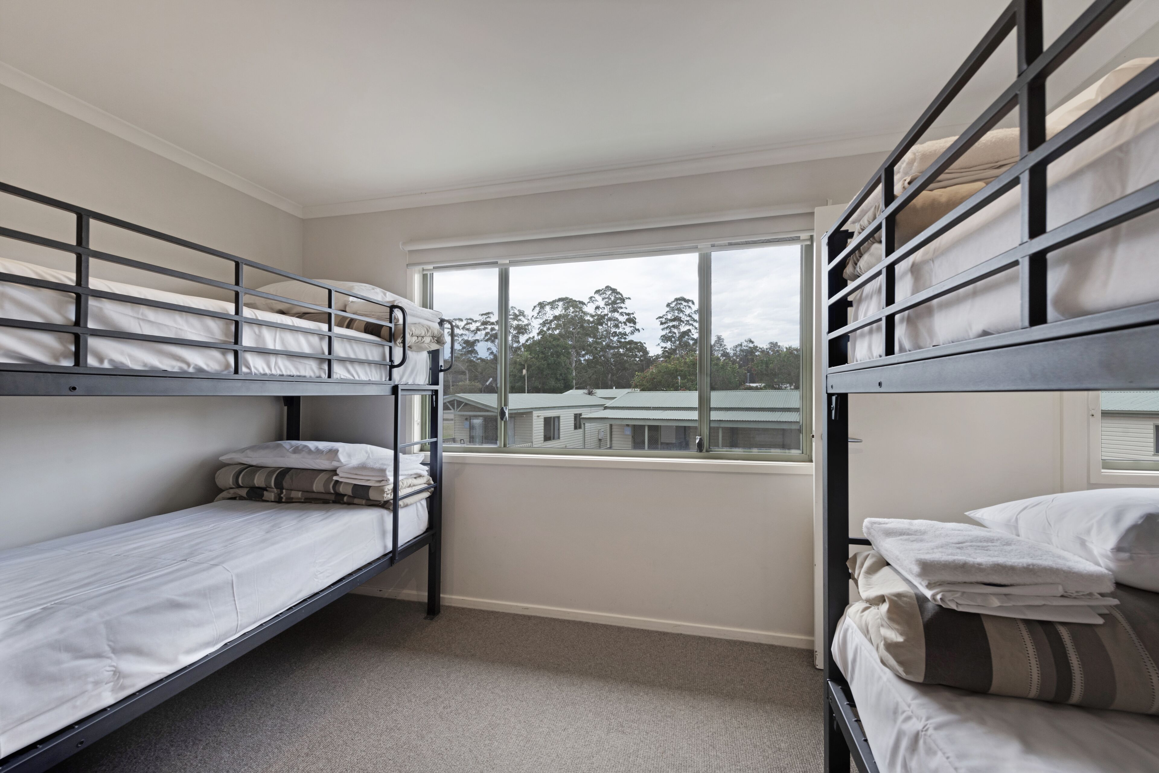 A room with two bunk beds, a window with a view of buildings, and a carpeted floor.