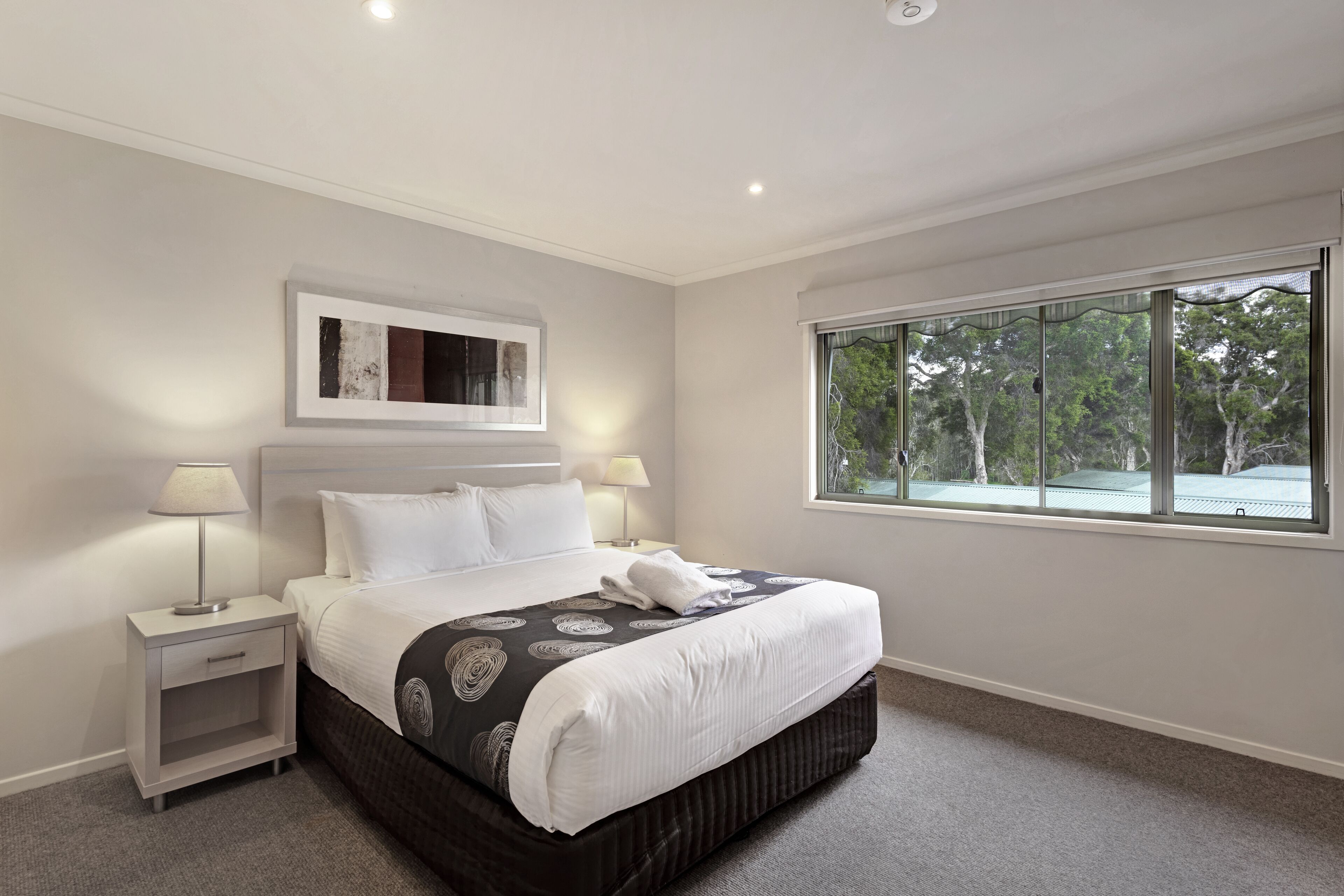 A hotel room with a large bed, two bedside tables, a window with a view of trees, and a ceiling light.