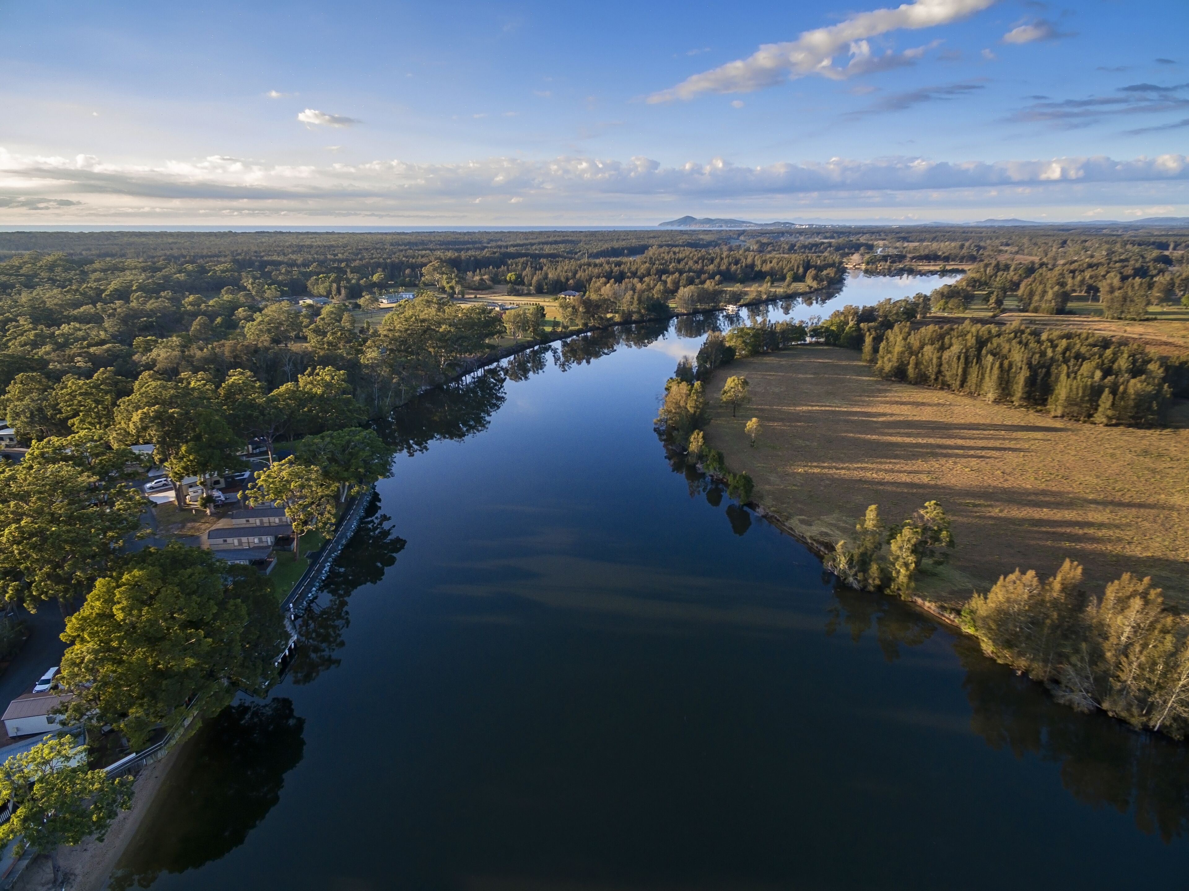 An aerial view of a river with surrounding greenery and a few buildings along the banks.