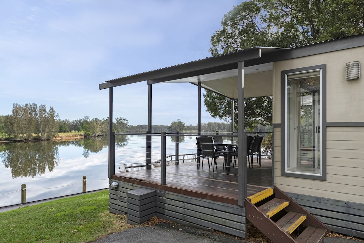 Una cabaña junto al lago con un porche, mobiliario exterior y vistas al lago.