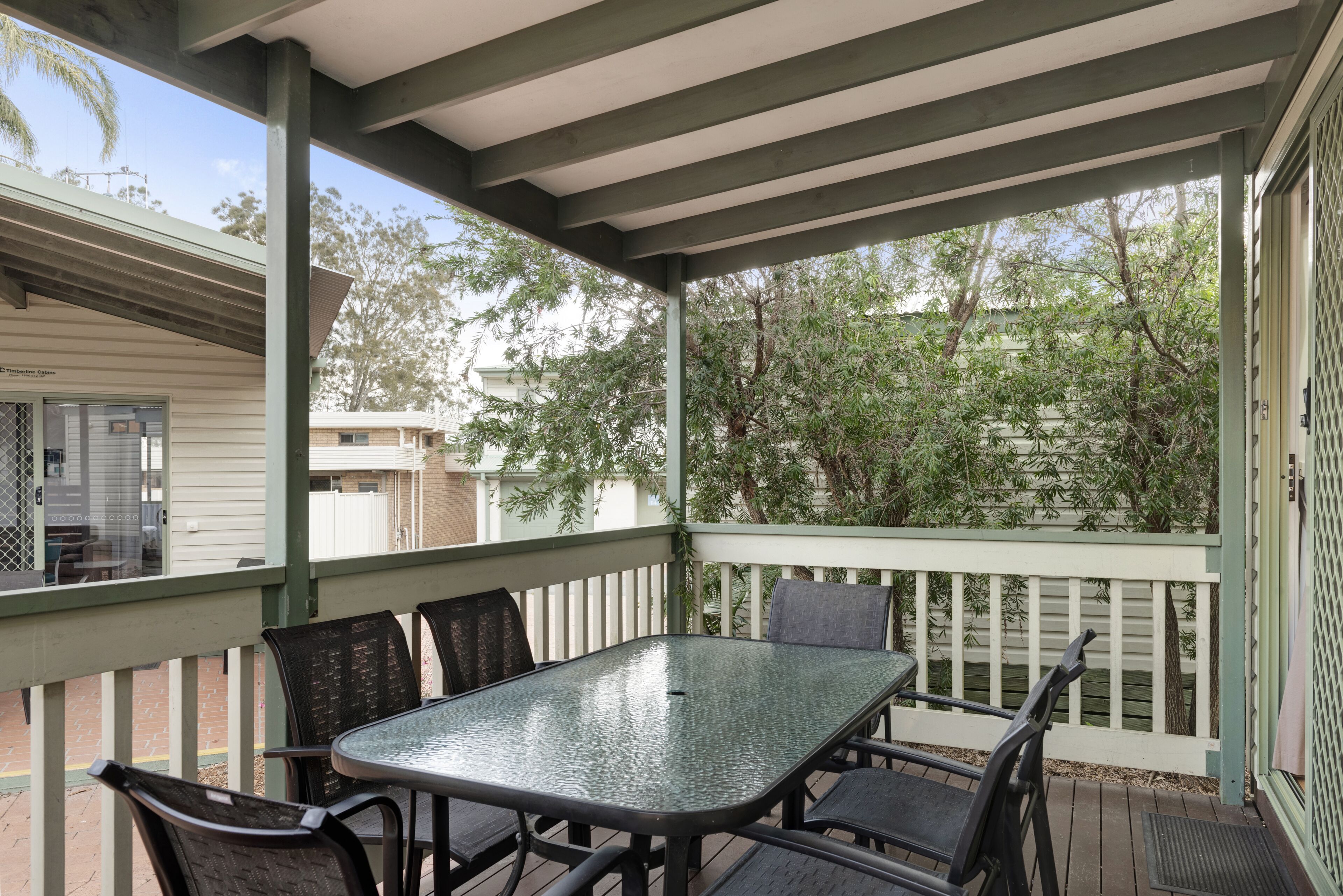 A covered outdoor patio with a table and chairs, surrounded by a white fence and trees.