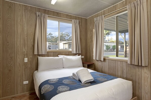 A bedroom with a large bed, wooden walls, and a view of the outdoors. - Discovery Parks - Forster (Darawank)