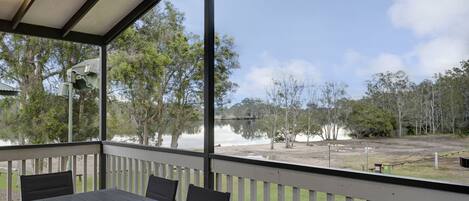 A covered outdoor area with a table and chairs, overlooking a body of water and trees.