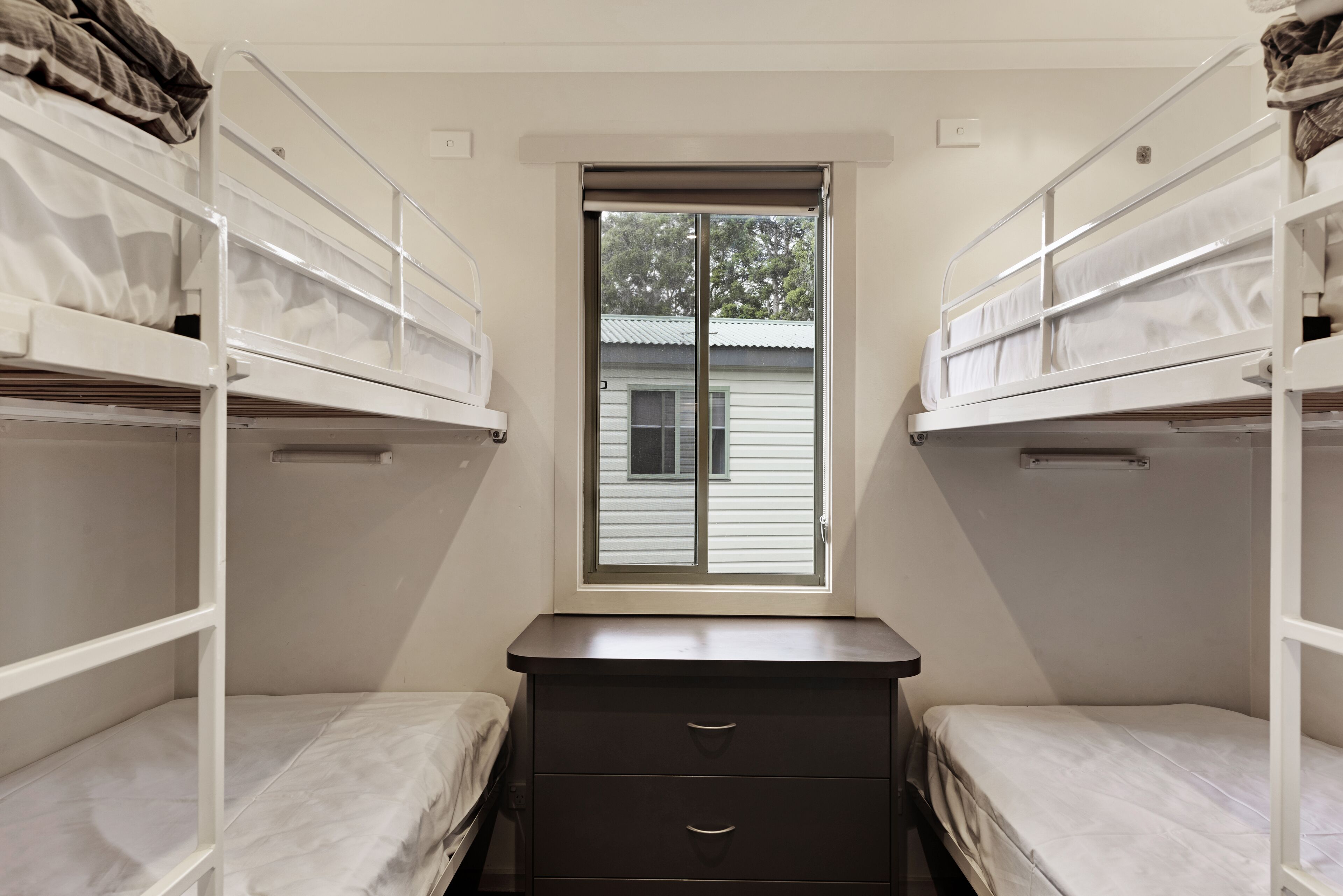 Un dormitorio con literas, un escritorio pequeño y una ventana con vista a una casa.