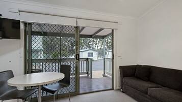A room with a sliding glass door leading to a balcony, a round table with two chairs, and a dark-colored sofa.