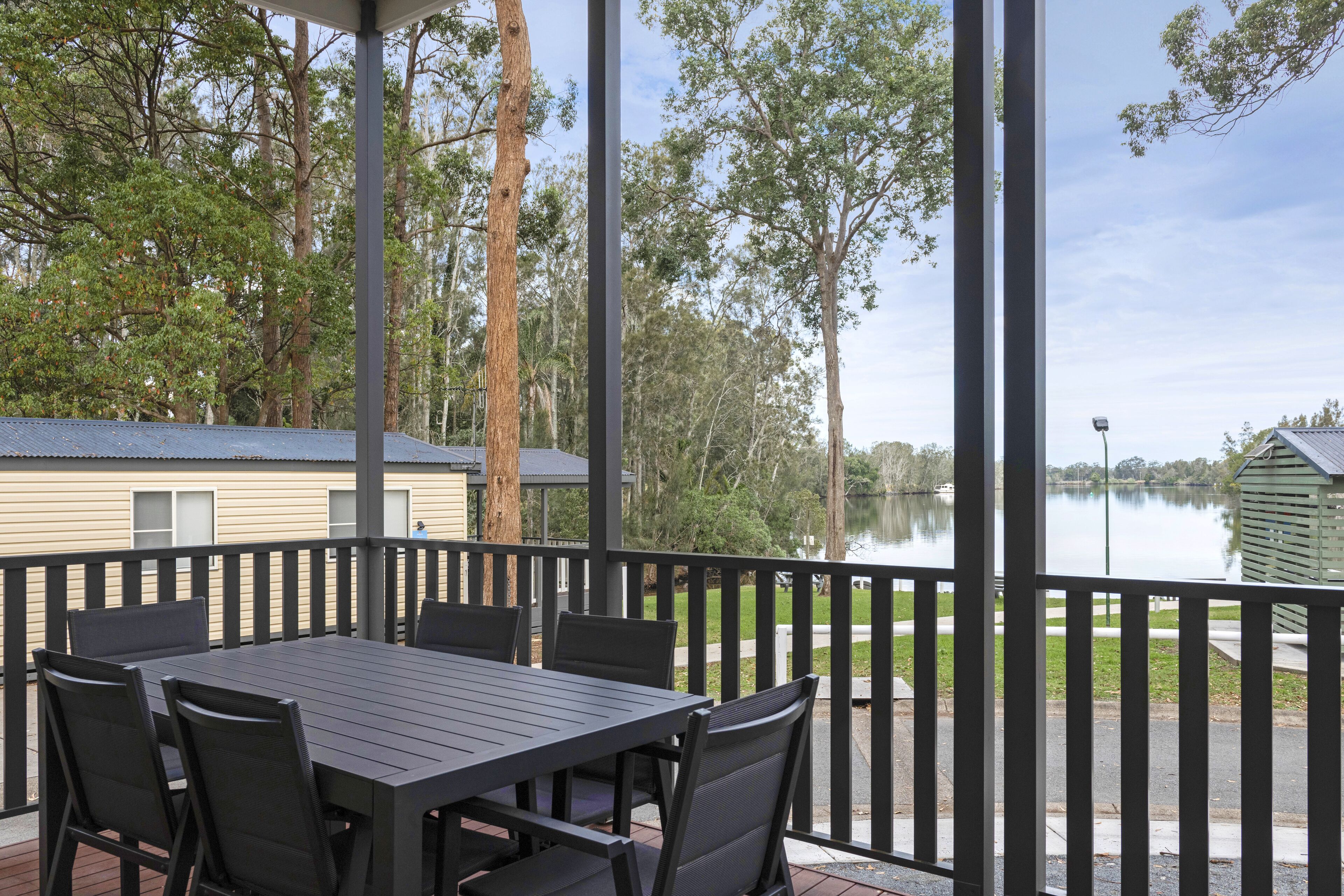 A covered outdoor area with a table and chairs, overlooking a lake and surrounded by trees.