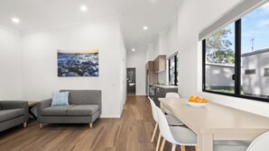 Un espace de vie et de salle à manger moderne, à aire ouverte, avec un canapé gris, une table à manger et des chaises, ainsi qu’une grande fenêtre donnant sur l’extérieur.