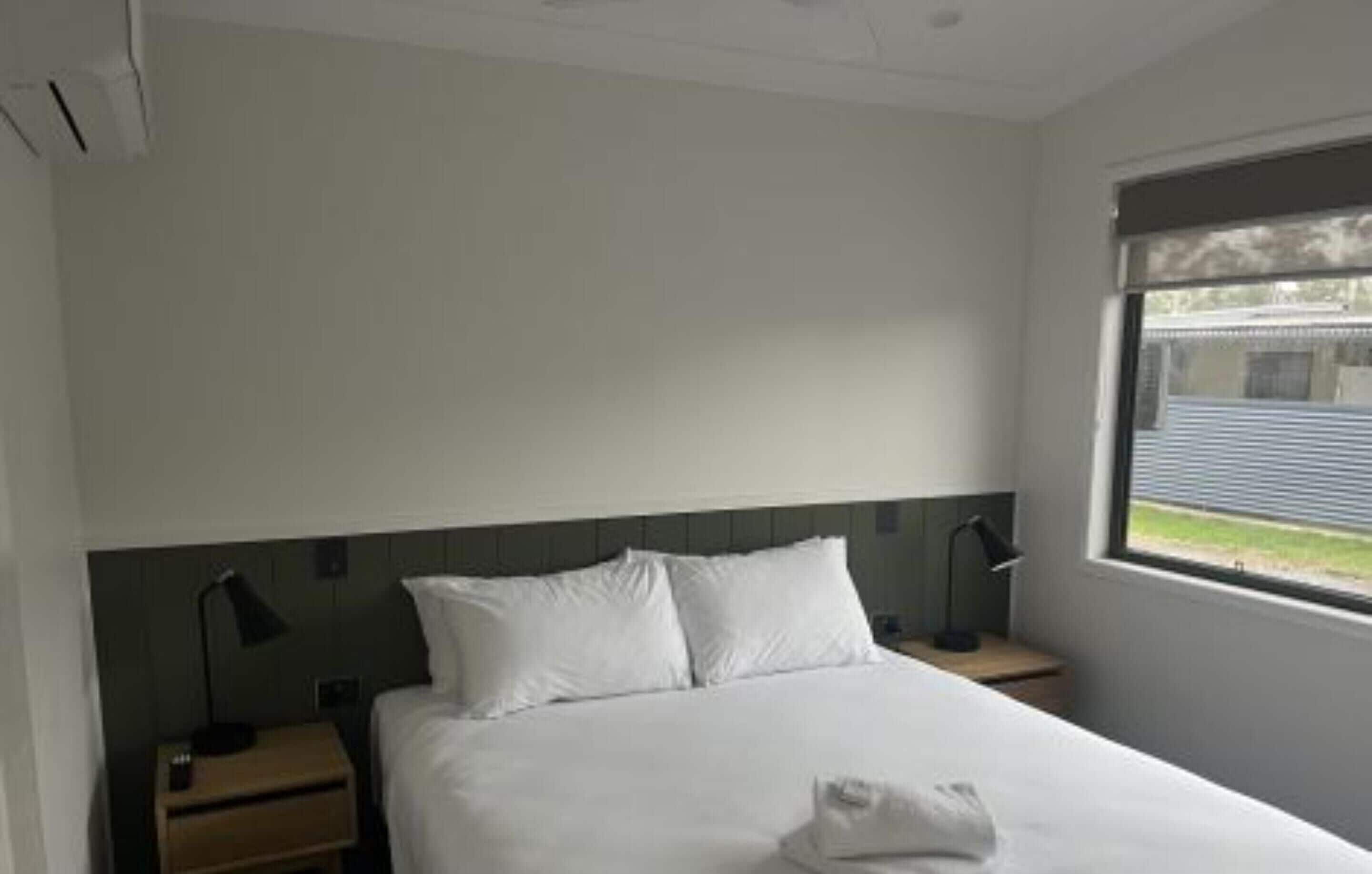 Ein Hotelzimmer mit einem Bett, zwei Nachttischen, einem Fenster und Blick ins Freie.