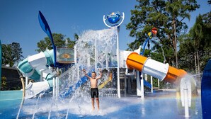Un espace de jeux aquatiques où un enfant se trouve au centre, entouré de jets d’eau et de toboggans.