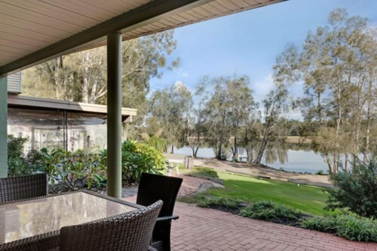 Un patio techado con mobiliario de mimbre, vista a un lago y un campo de golf al fondo.