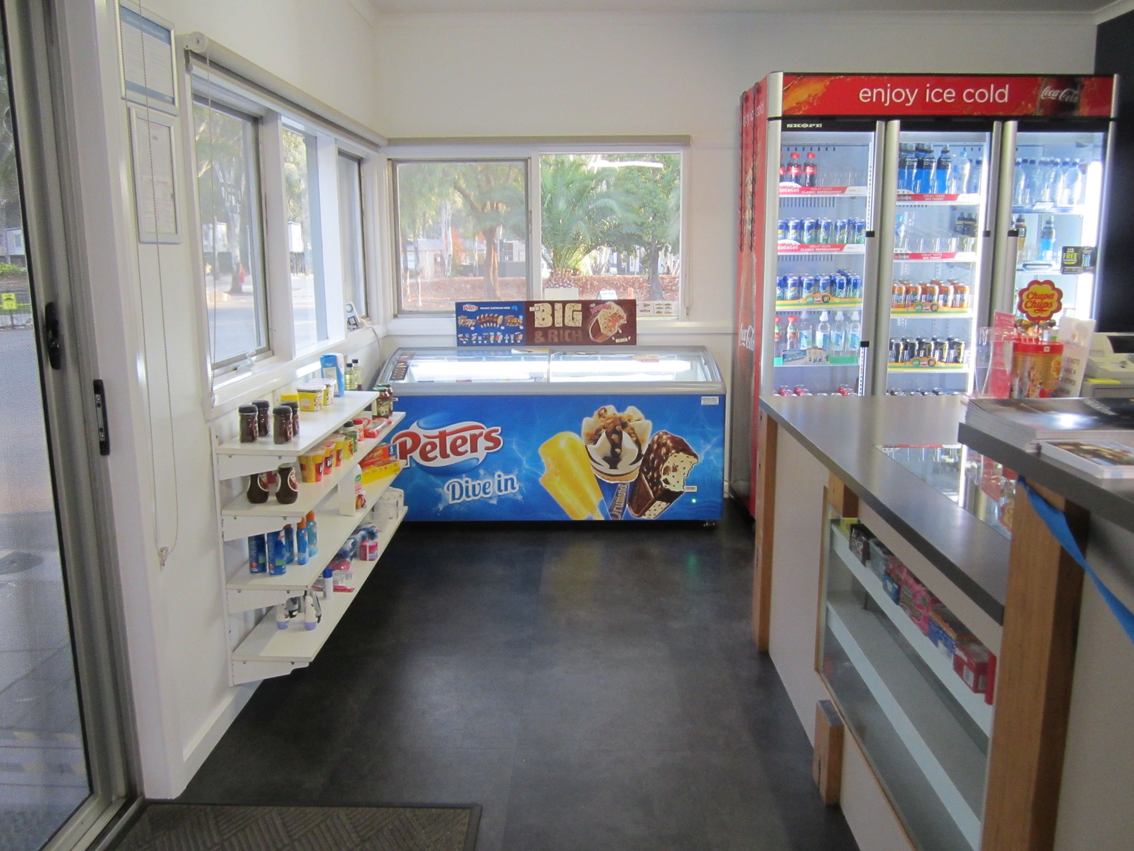 A small ice cream shop with a 'Peters Dive in' freezer, shelves stocked with various ice cream products, and a Coca-Cola cooler.