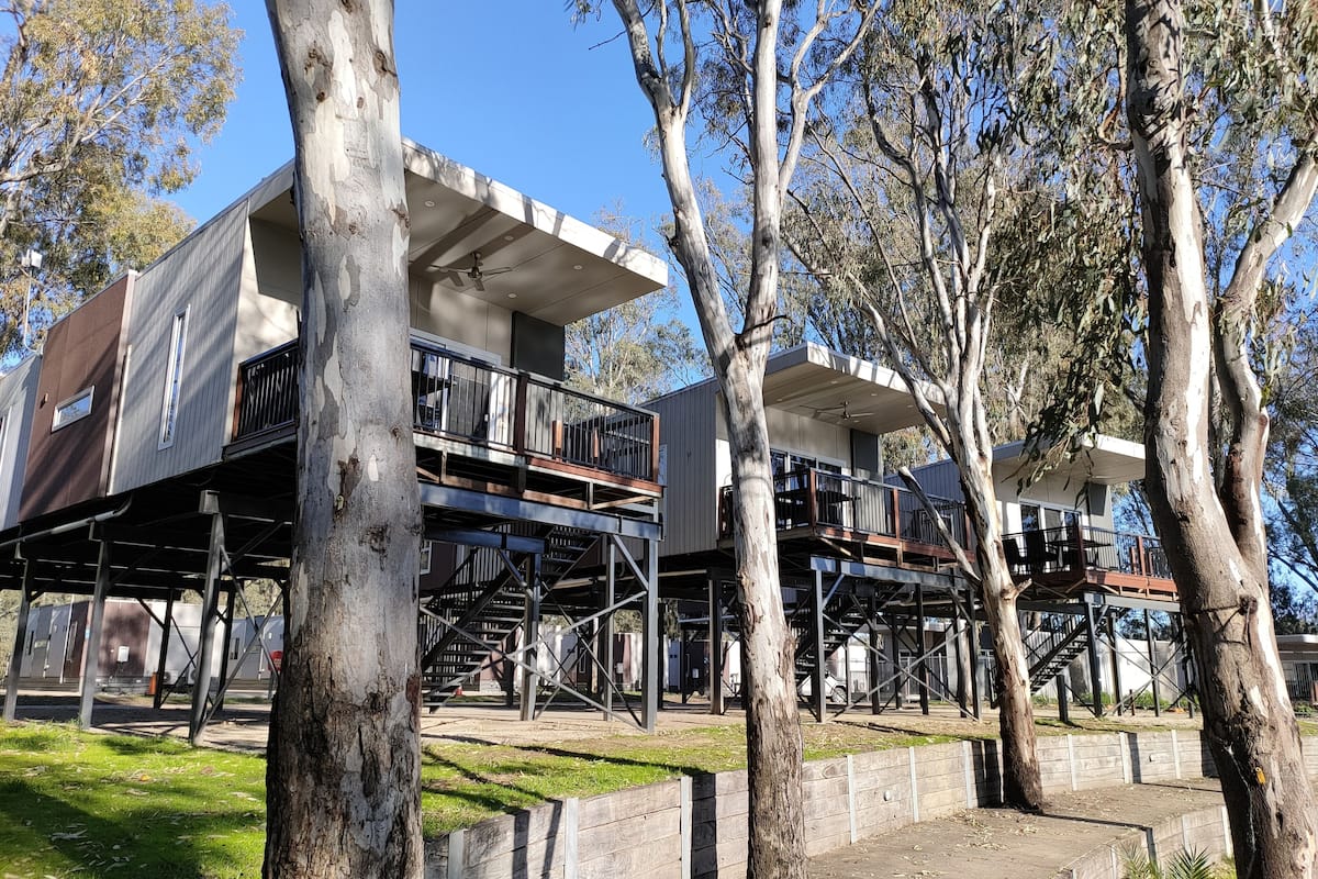 A modern two-story building with a balcony and a flat roof, surrounded by trees.