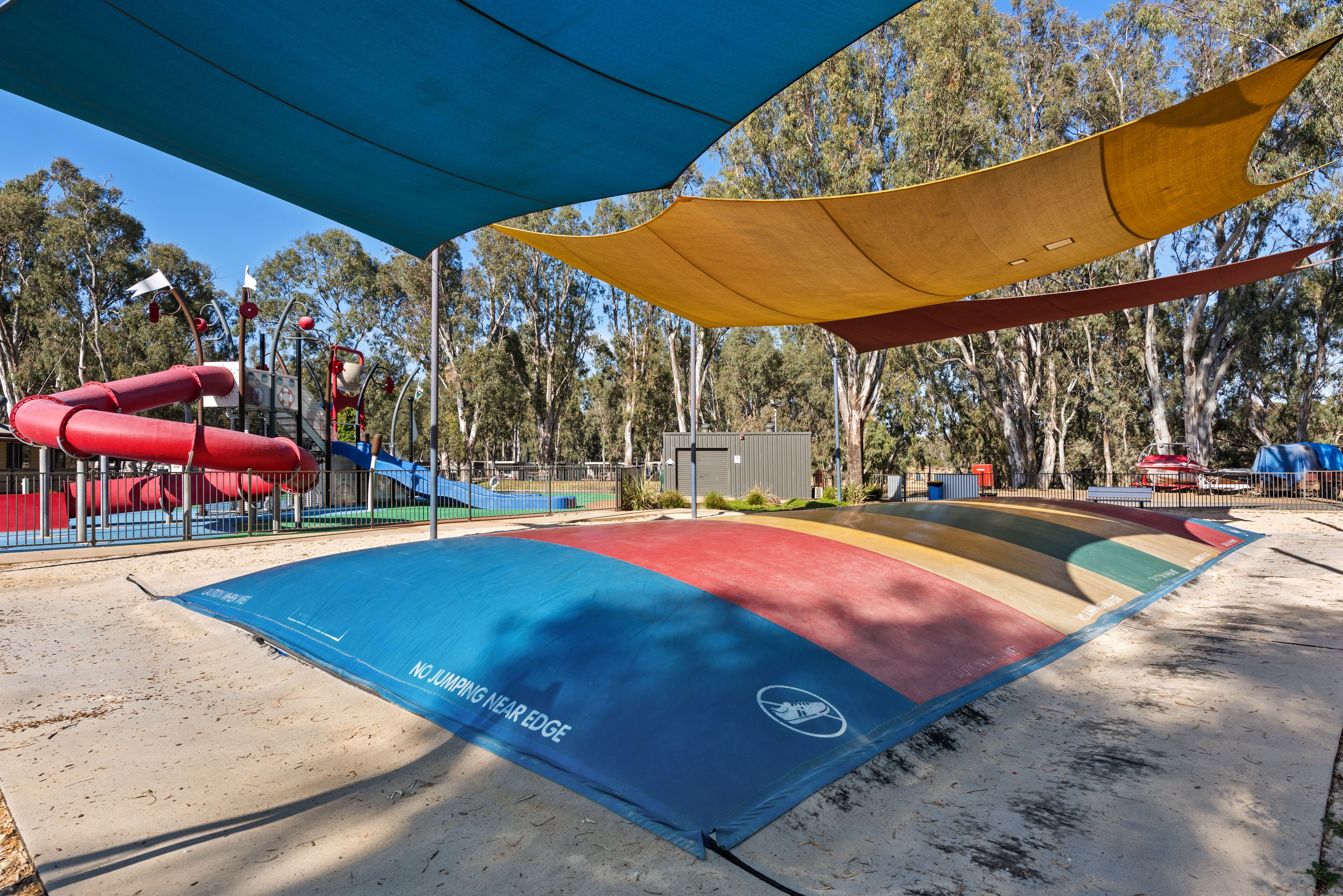 A playground with a red slide, a blue climbing net, and a yellow canopy.