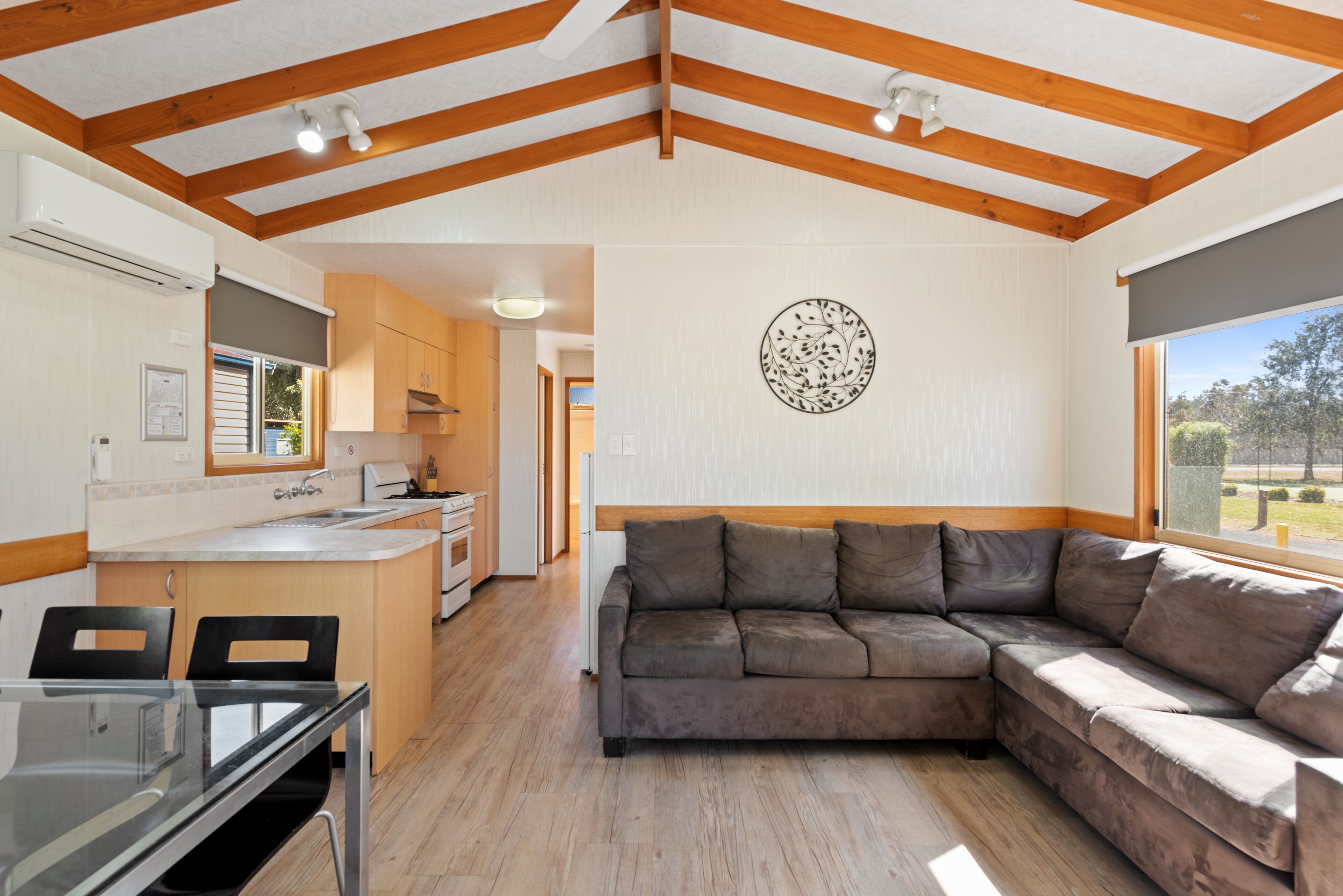Una cocina moderna con vigas de madera, una zona de comedor con una mesa de vidrio y un amplio sofá en forma de L.