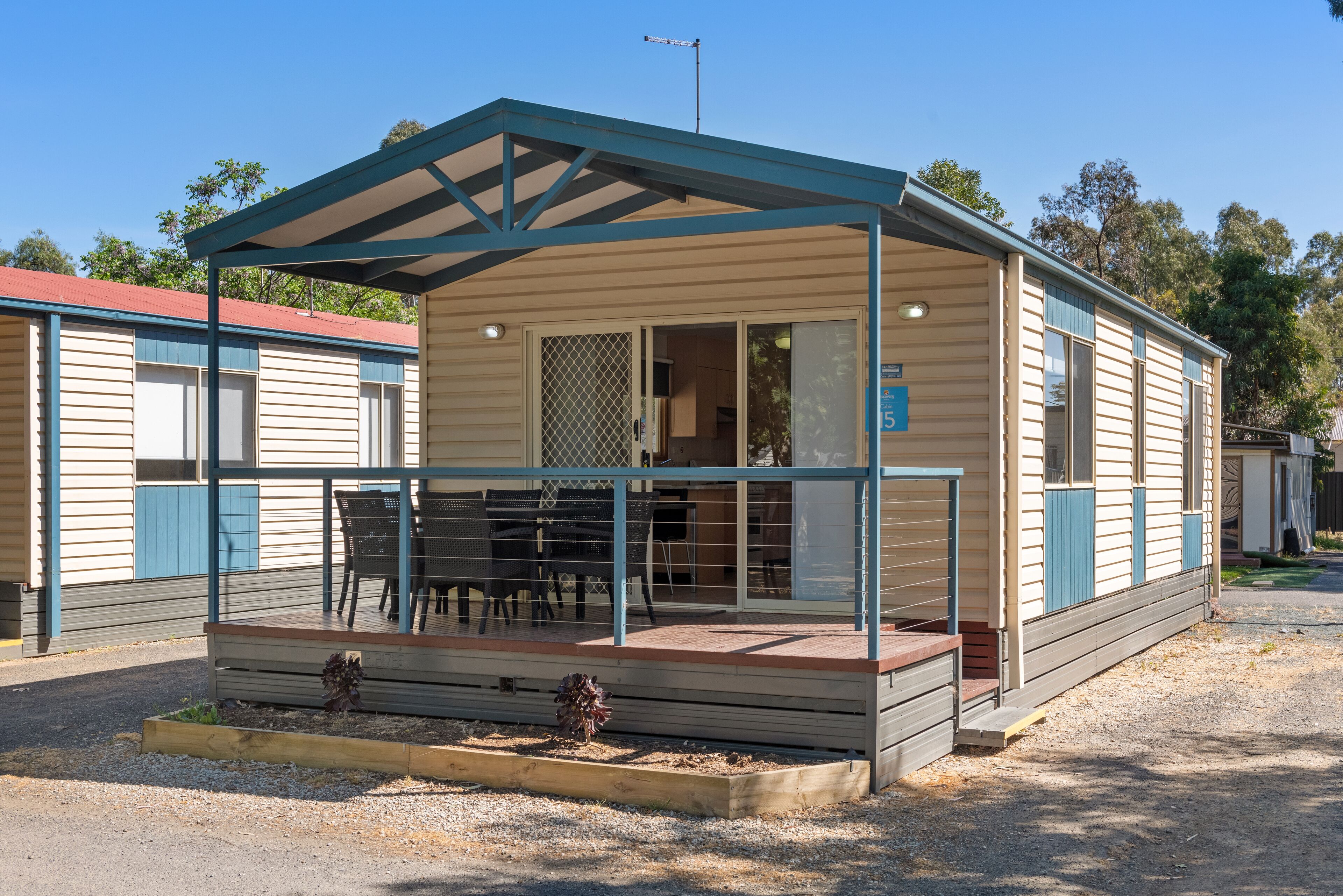A single-story mobile home with a covered porch, a fenced patio area, and a small garden bed.
