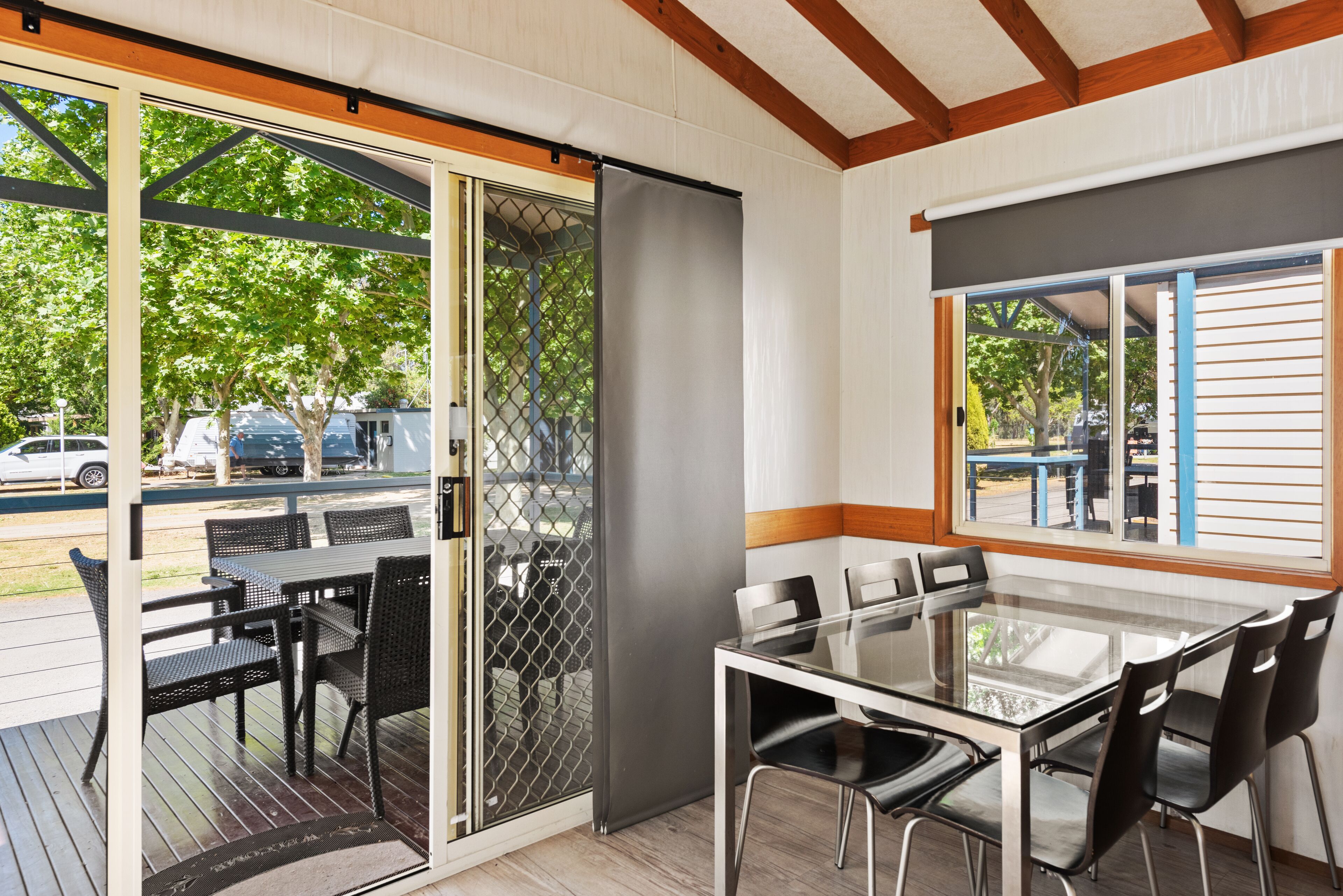 A covered outdoor dining area with a glass table and chairs, a sliding glass door, and a view of the street.