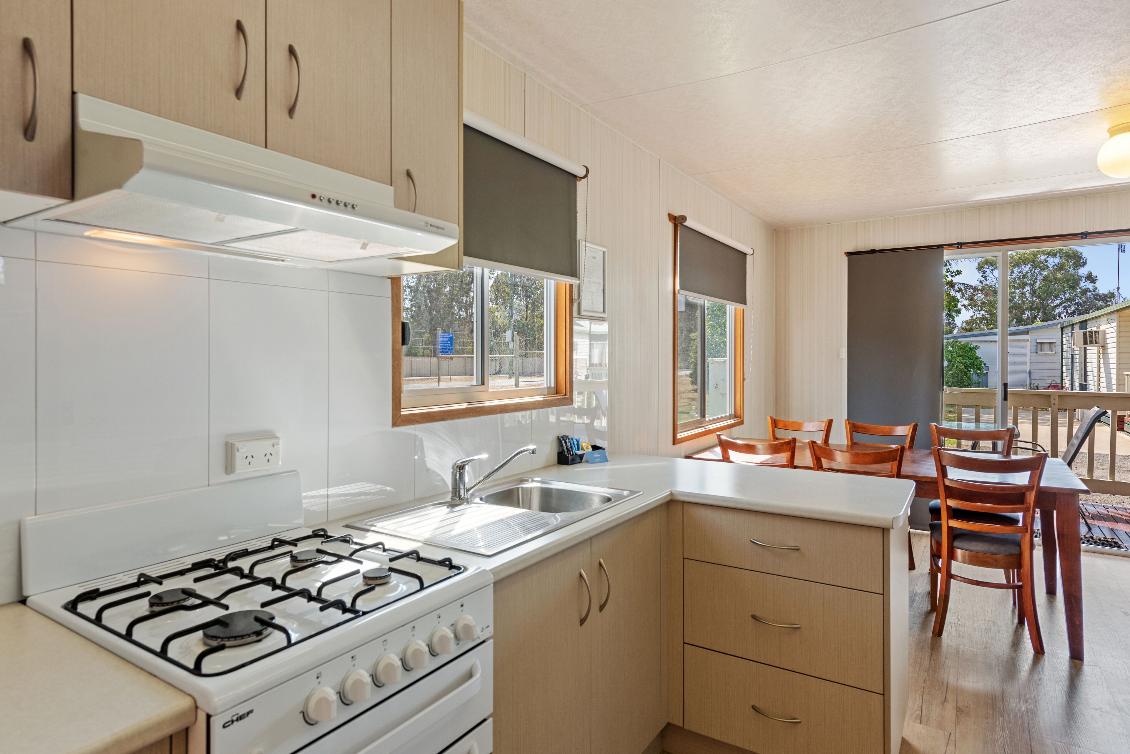A modern kitchen with white cabinets, a gas stove, and a sink. There is a dining area with wooden chairs and a table.