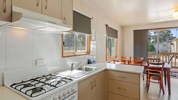 Cocina moderna con armarios blancos, estufa a gas y un lavamanos. Hay un comedor con sillas de madera y una mesa.