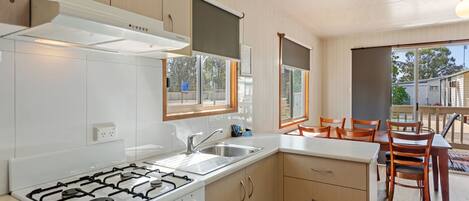 A modern kitchen with white cabinets, a gas stove, and a sink. There is a dining area with wooden chairs and a table.