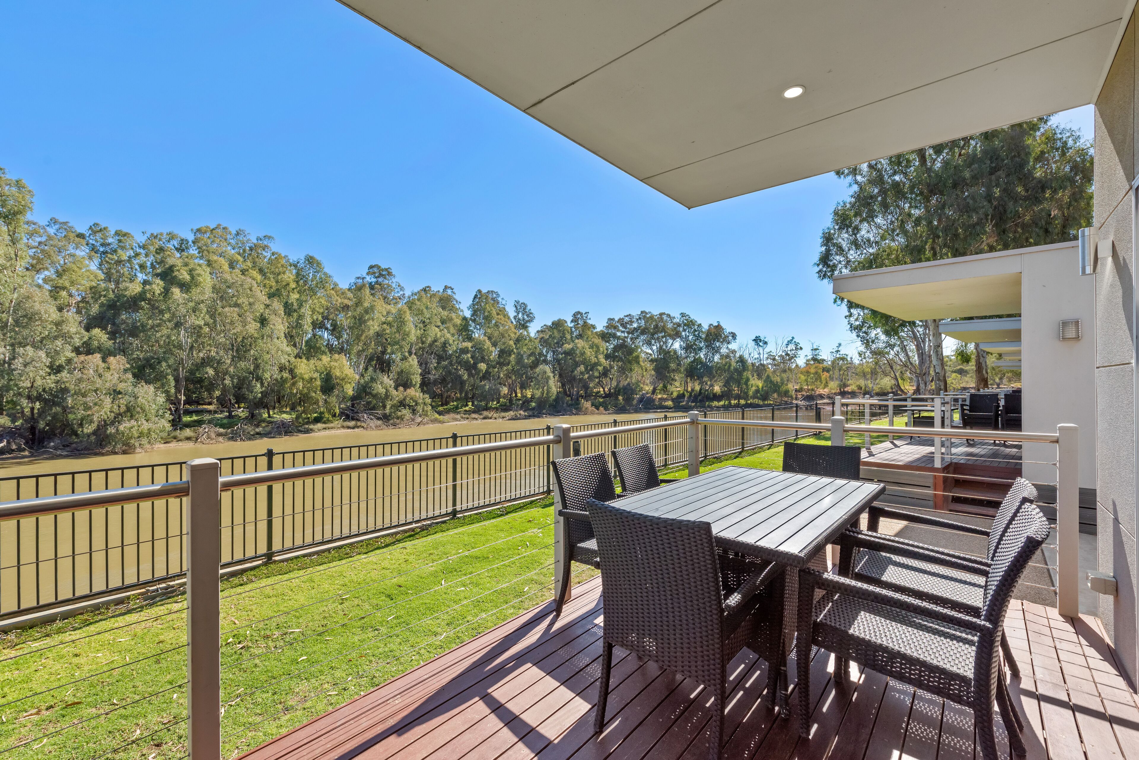 A deck with a table and chairs, overlooking a river and greenery.