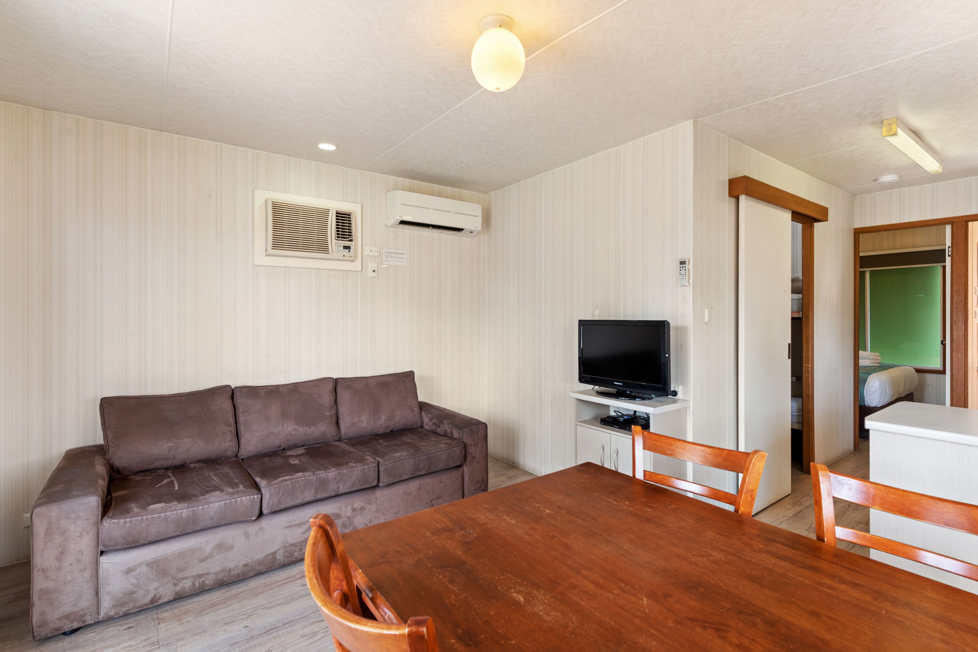 A living room with a brown sofa, a wooden dining table, and a television on a stand.