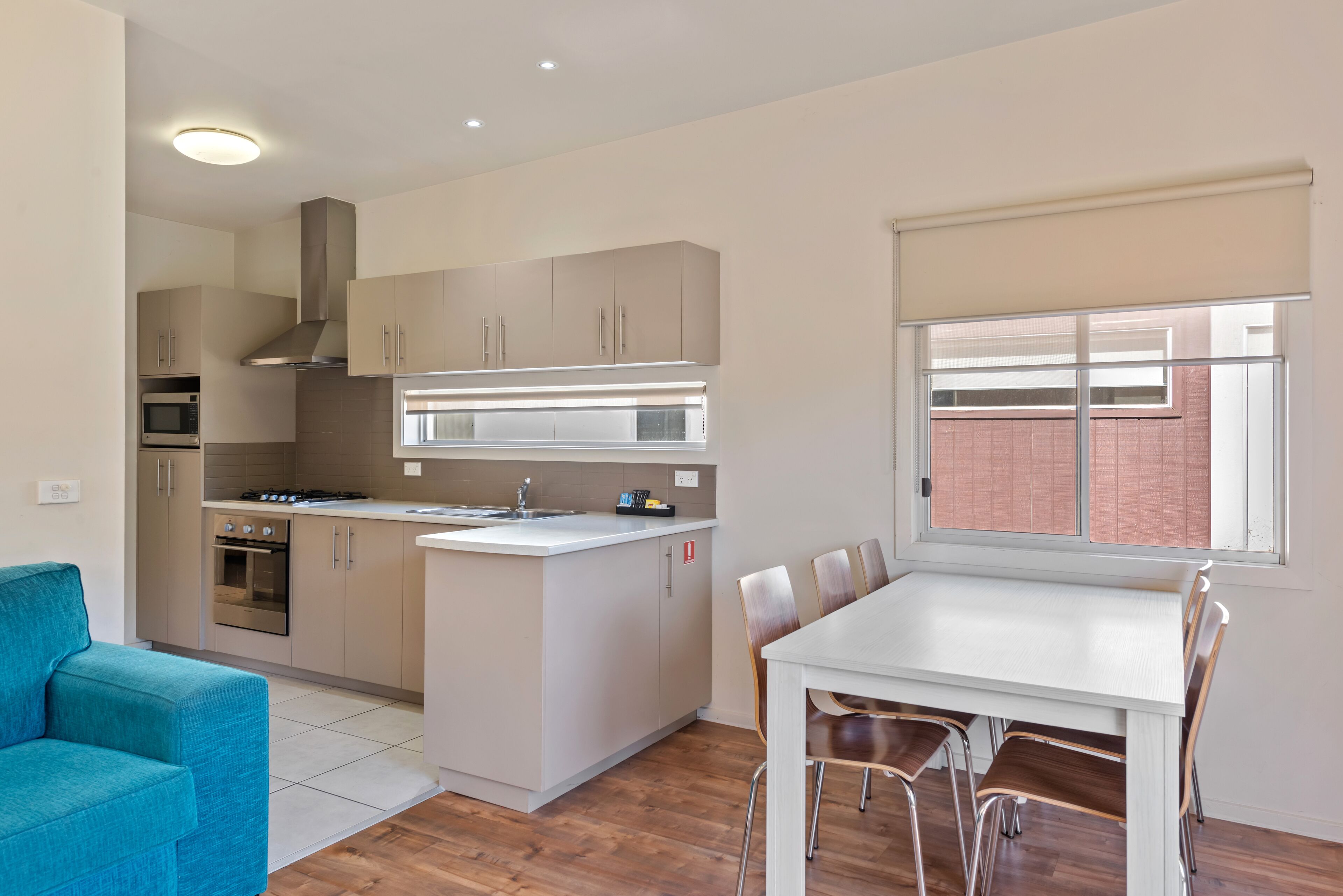 A modern kitchen with a central island, built-in oven, and microwave. There is a dining area with a white table and chairs.