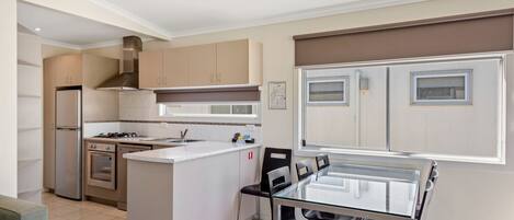 Una cocina moderna con electrodomésticos de acero inoxidable, una mesa de comedor de vidrio y un ventanal con persianas.