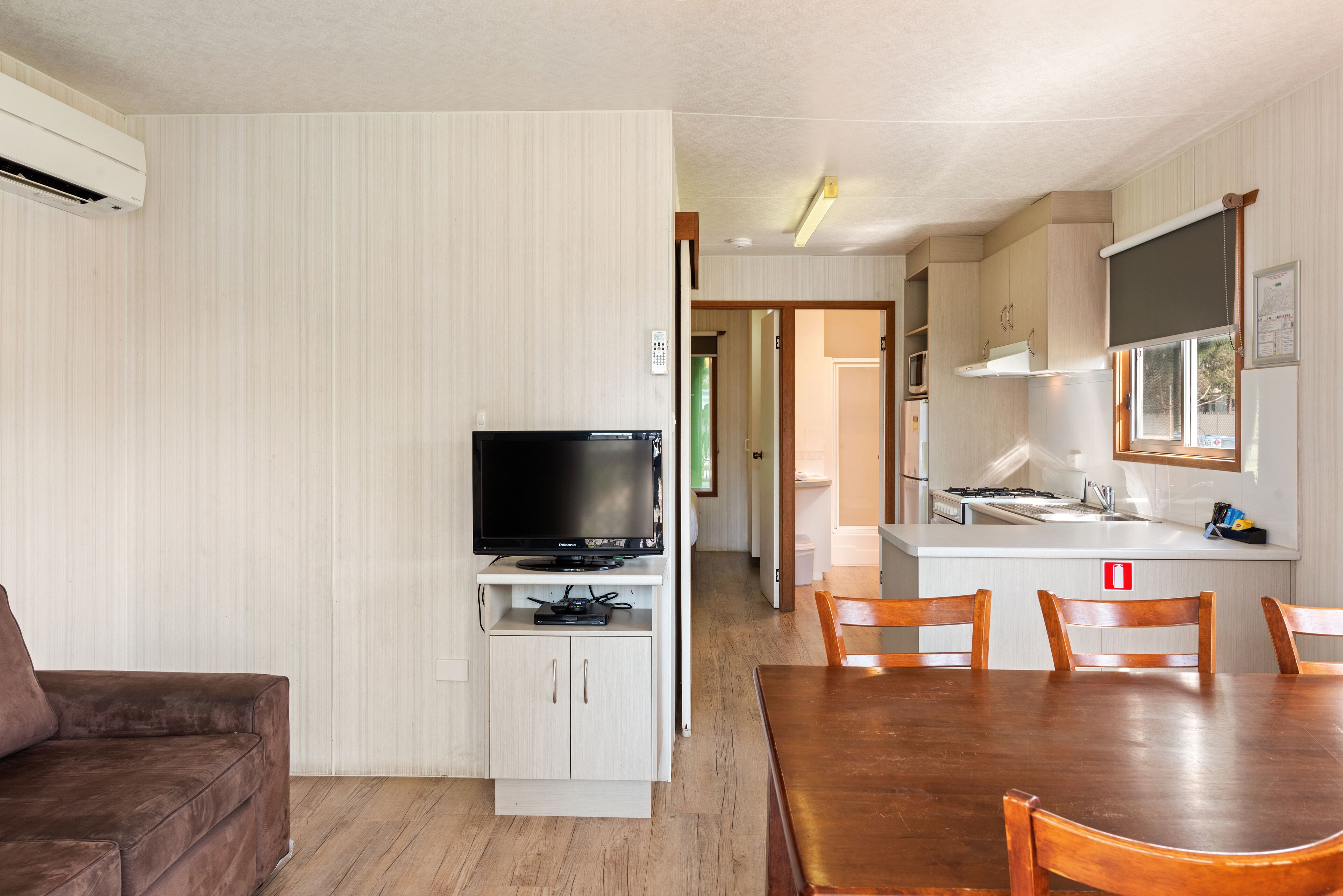 Un espacio habitable compacto con un televisor sobre un mueble, una mesa de comedor con sillas y una zona de kitchenette.