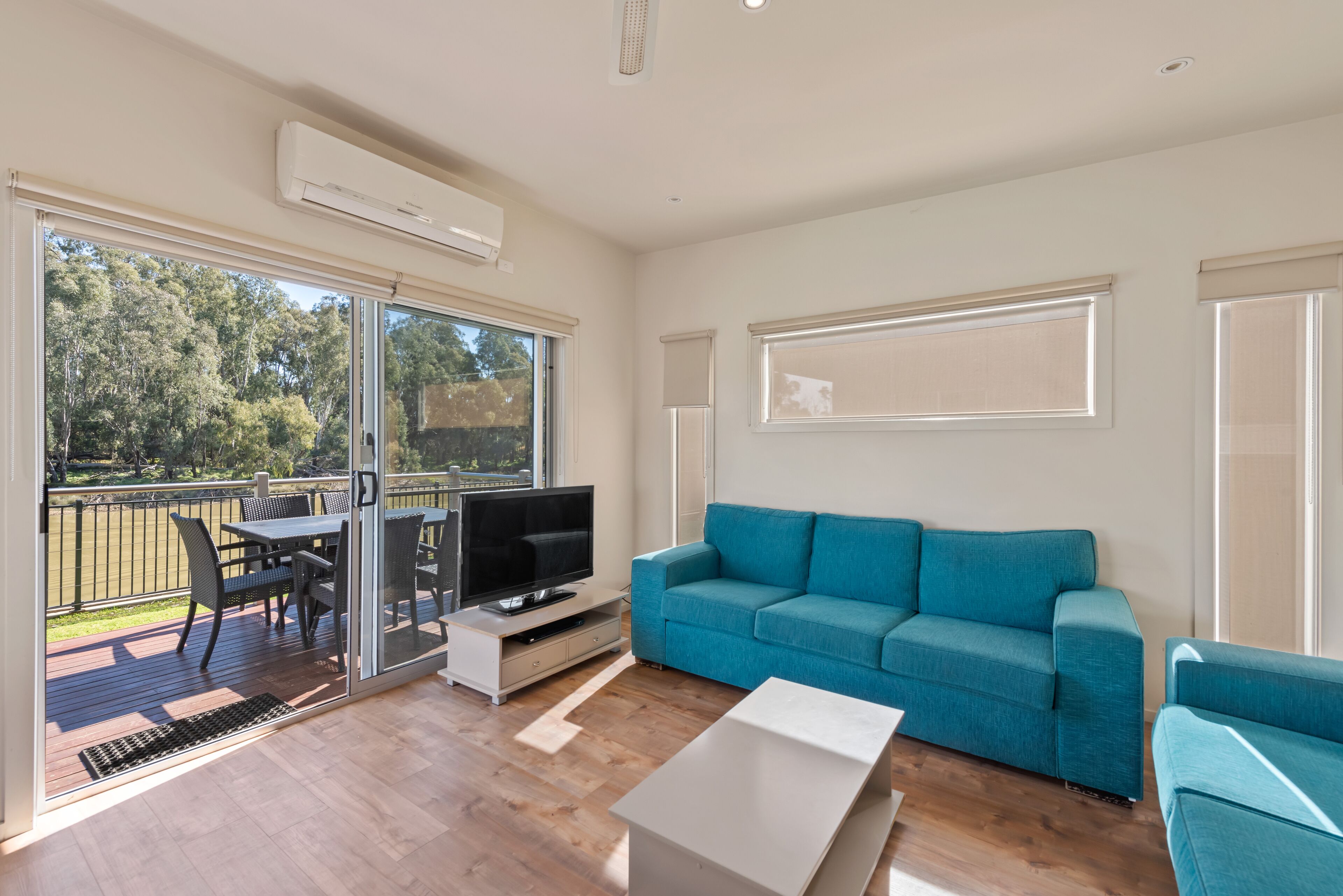 Una sala de estar moderna con un sofá color turquesa, un televisor de pantalla plana y un ventanal de vidrio que da a una terraza al aire libre.