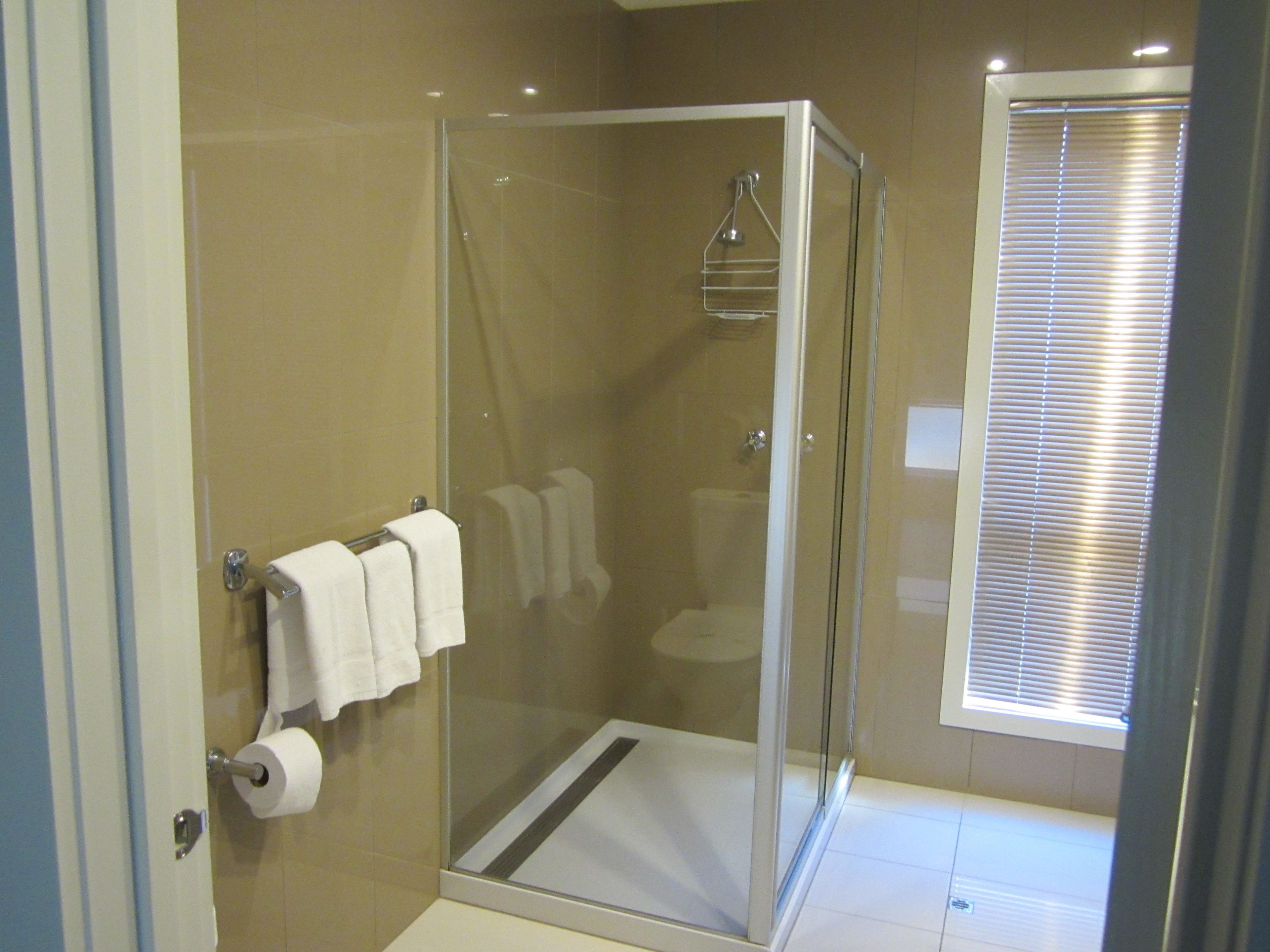 Un baño moderno con ducha envuelta en vidrio, inodoro y ventana con persianas.