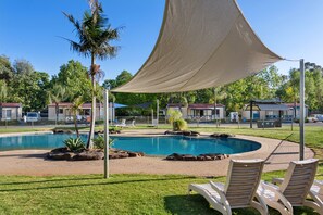 Relax by the pool surrounded by lush greenery and shaded by a large canopy.