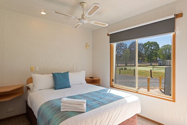 Un dormitorio con una cama grande, un ventilador de techo, una ventana con vistas al exterior y una mesita de noche de madera.
