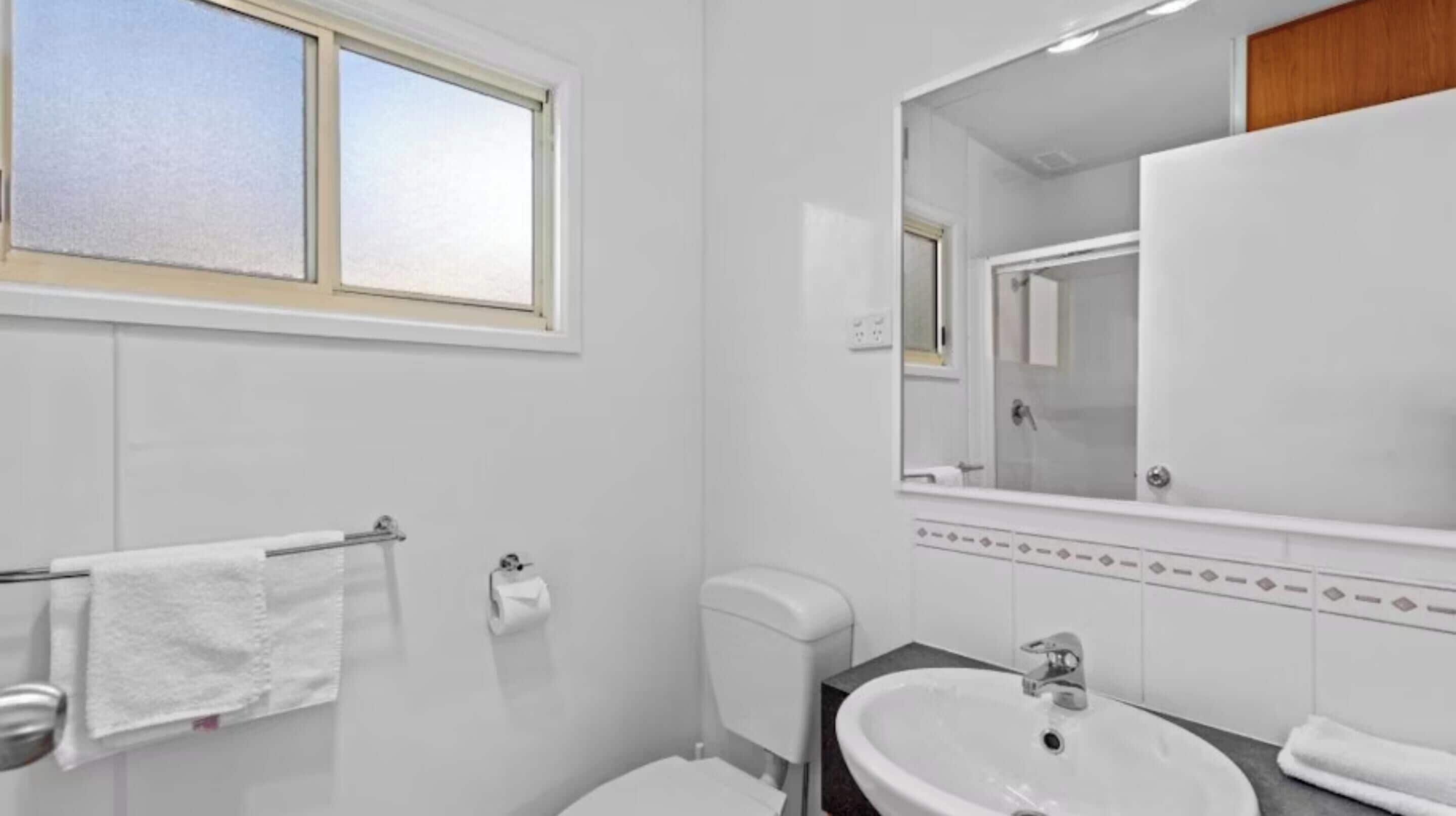 Un baño moderno con inodoro, lavabo y un espejo grande.