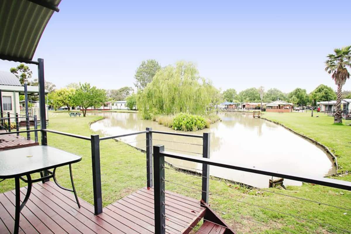 A deck with a table and chairs overlooking a pond with a willow tree in the center.