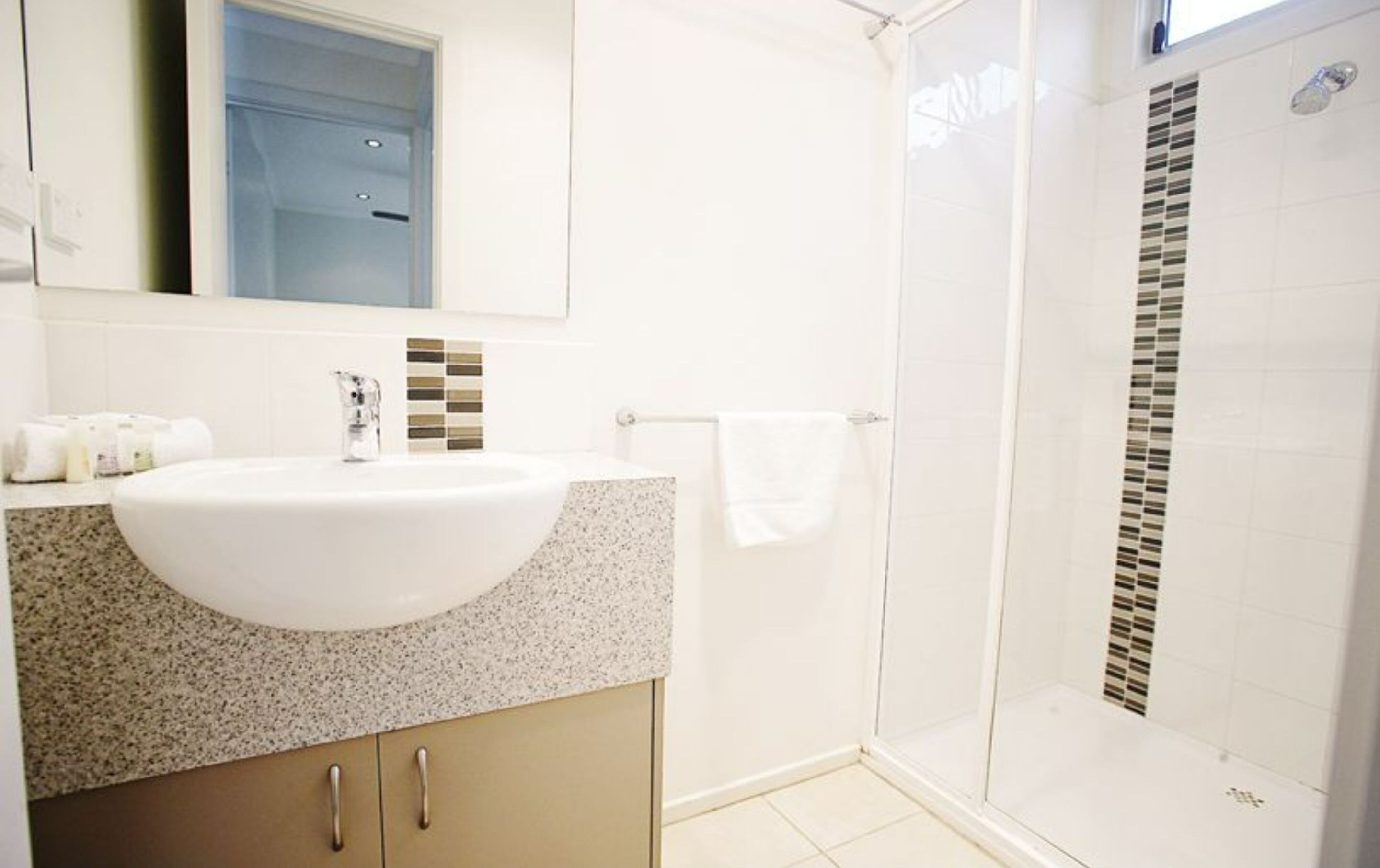 A bathroom with a white sink, a mirror, a shower, and a towel rack.
