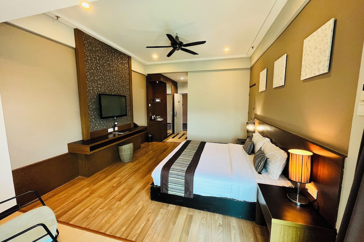 A modern hotel room with a large bed, a television, a ceiling fan, and a wooden floor.