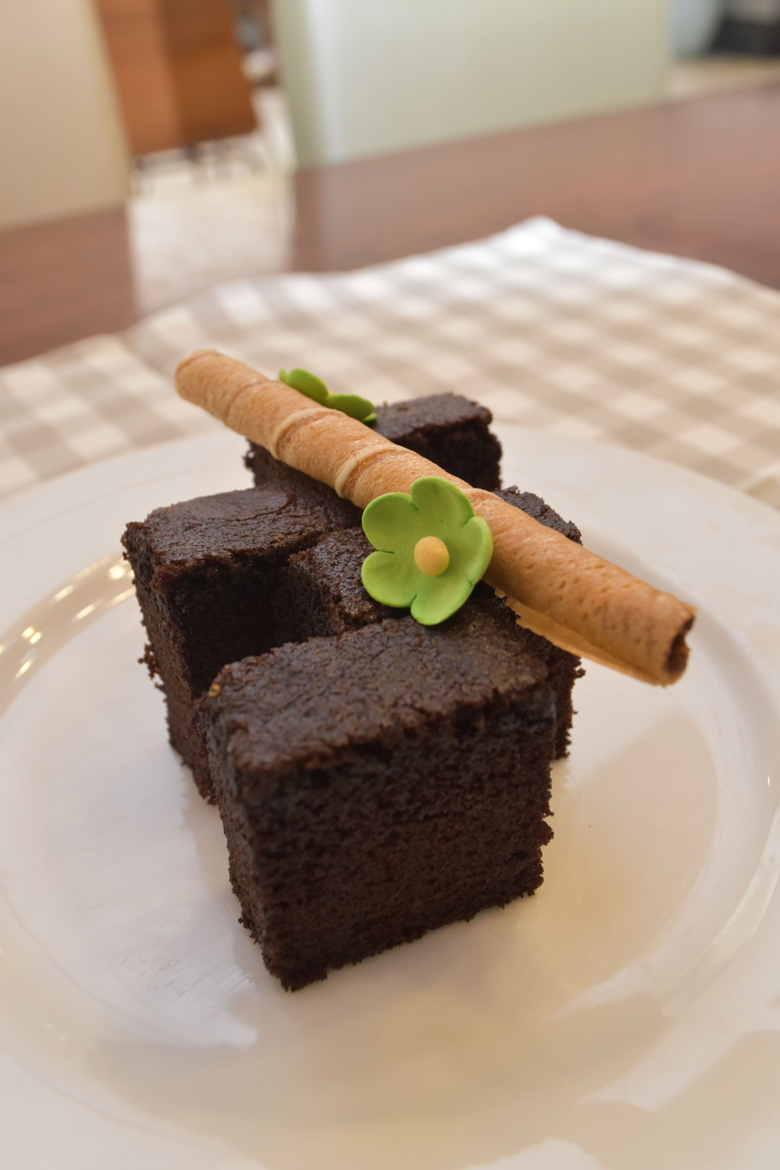 A plate with three square pieces of chocolate cake, each topped with a green leaf and a cinnamon stick.