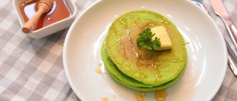 Une assiette de crêpes vertes, nappées de miel et garnies d’une noisette de beurre, servies sur une assiette blanche posée sur une nappe à carreaux.