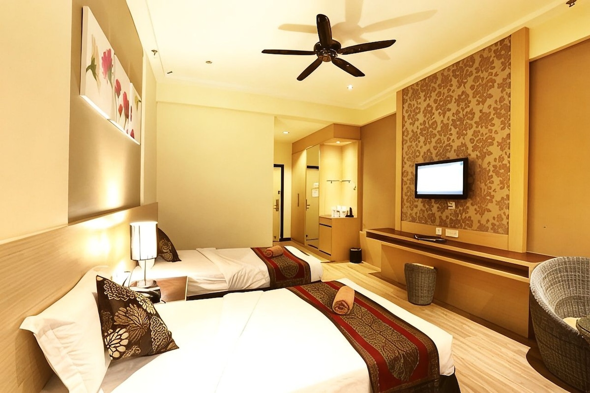 A hotel room with two beds, a ceiling fan, a television, and a small seating area.