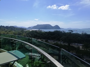 Ein Balkon mit Glasgeländer mit Blick auf eine Küstenlandschaft, Berge und Boote.